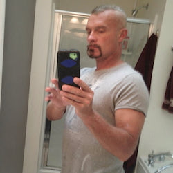 Man taking a mirror selfie wearing a gray t-shirt in a room.