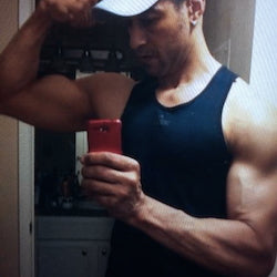 Muscular man taking a mirror selfie wearing a black tank top.