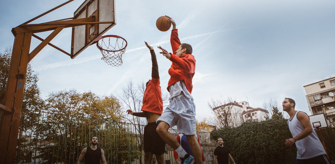A group of men playing basketball on a court in the city with one man getting ready to dunk it as another tries to block him