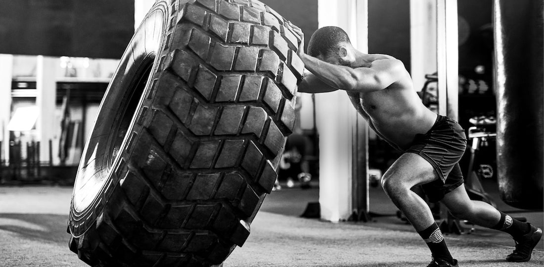 A muscular man in workout shorts with no shirt on flipping a giant tire for a workout