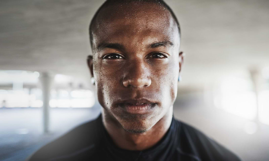 A black man with an athletic build staring intently with sweat on his face from working out