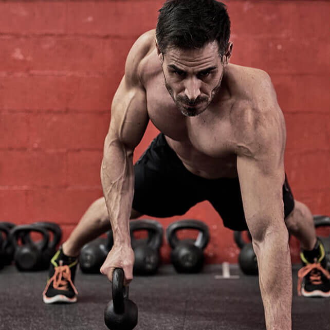 Man exercising with a kettlebell against a red brick wall.