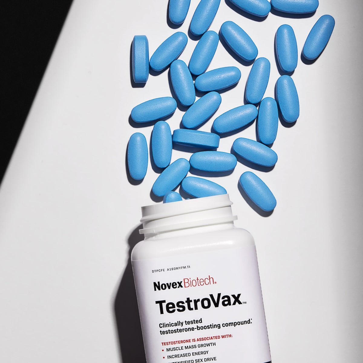 An open bottle of Novex Biotech TestroVax spills bright blue tablets onto a white surface, highlighting the supplement’s dosage form.