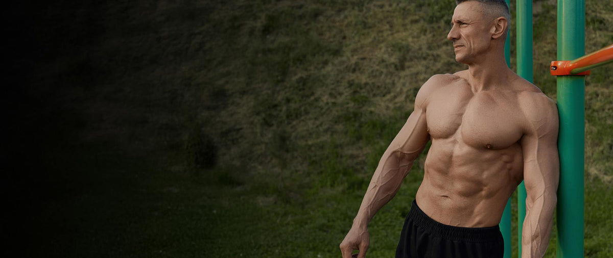 Man with a muscular build standing outdoors on a grassy area.