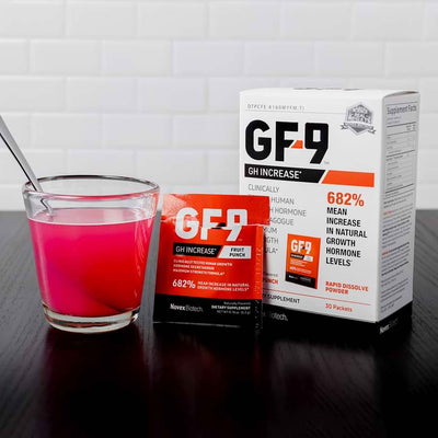 Glass of pink liquid with spoon for stirring, alongside GF-9 Fruit Punch Powder 30 packet box and opened single-serve packet