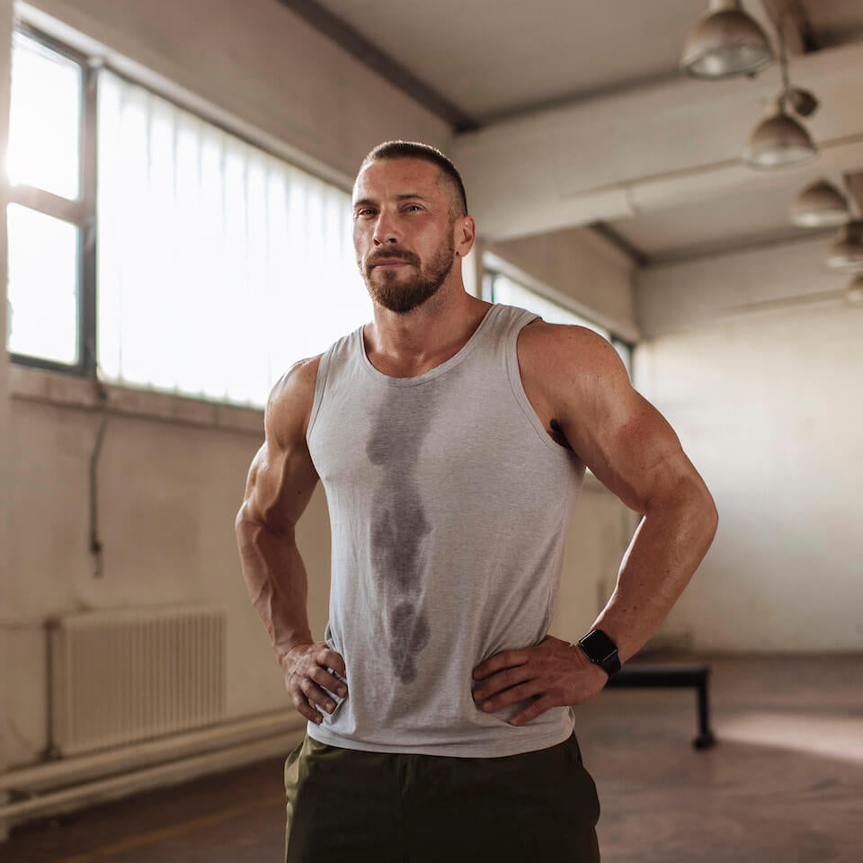 Muscular white man in a sweat-covered tank top standing with his hands on his hips